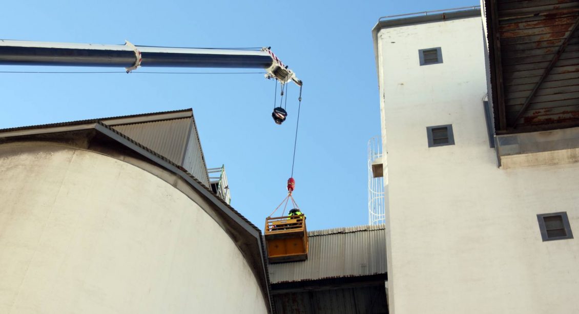 Crane lifting tradesman to seal silo roof