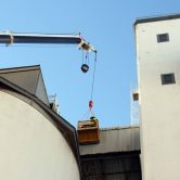 Crane lifting tradesman to seal silo roof